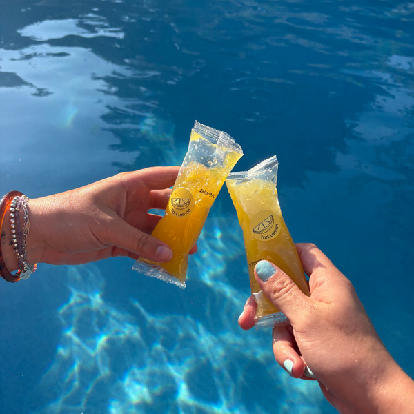 Two hands holding Sleet Pops together over a sunny blue swimming pool background.
