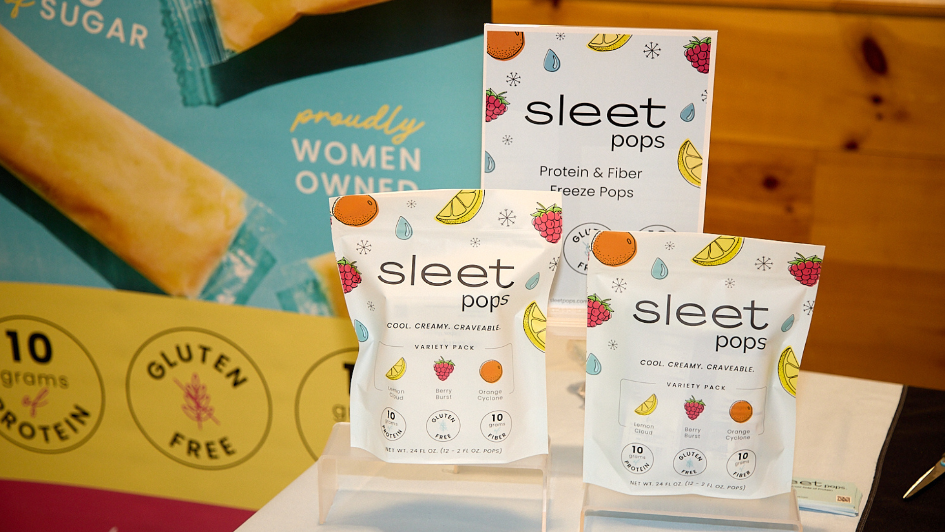 Sleet Pops protein and fiber freeze pops packaging on a wooden surface with branded boxes in the background. 
