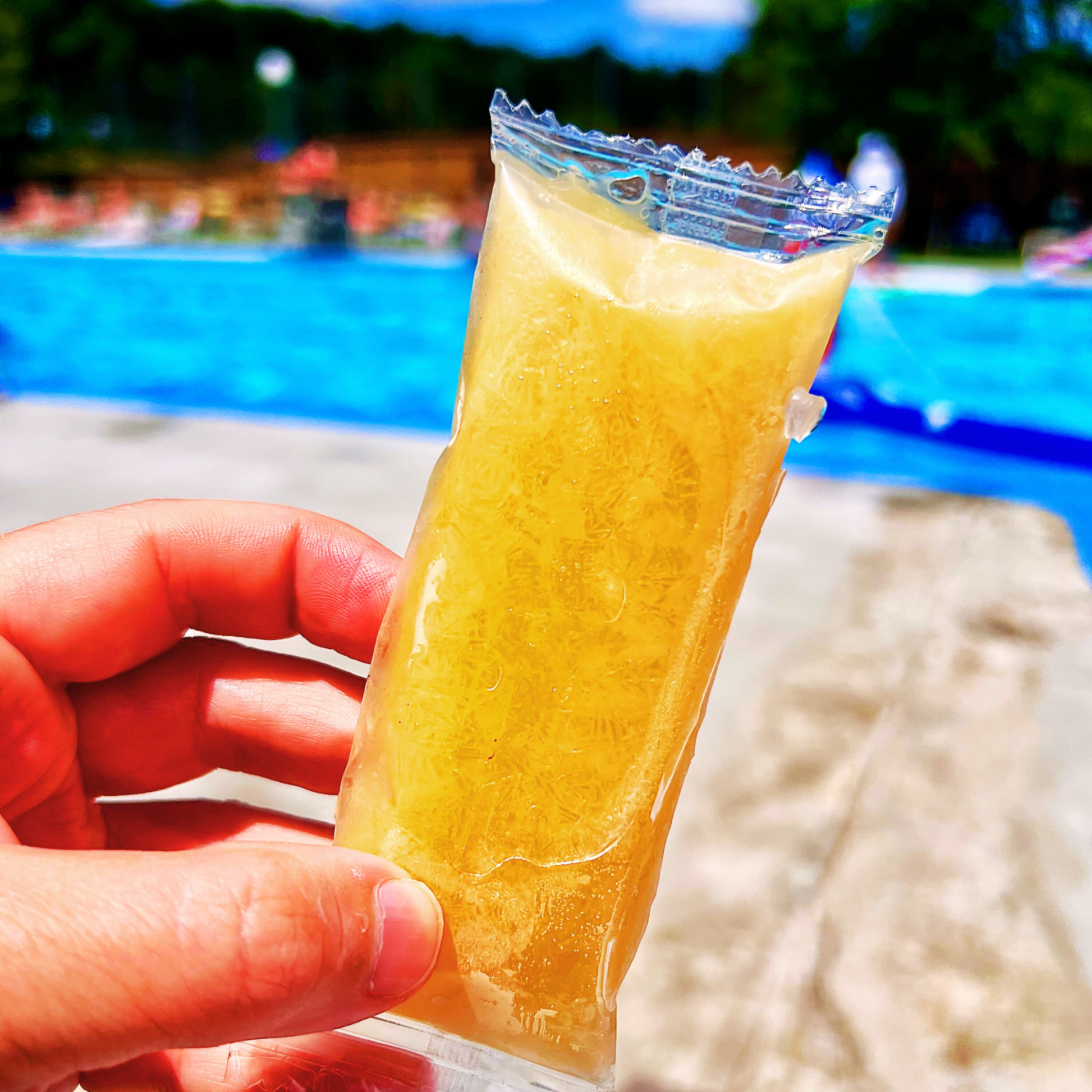 Hand holding a Sleet Pop by a pool with a blurred background