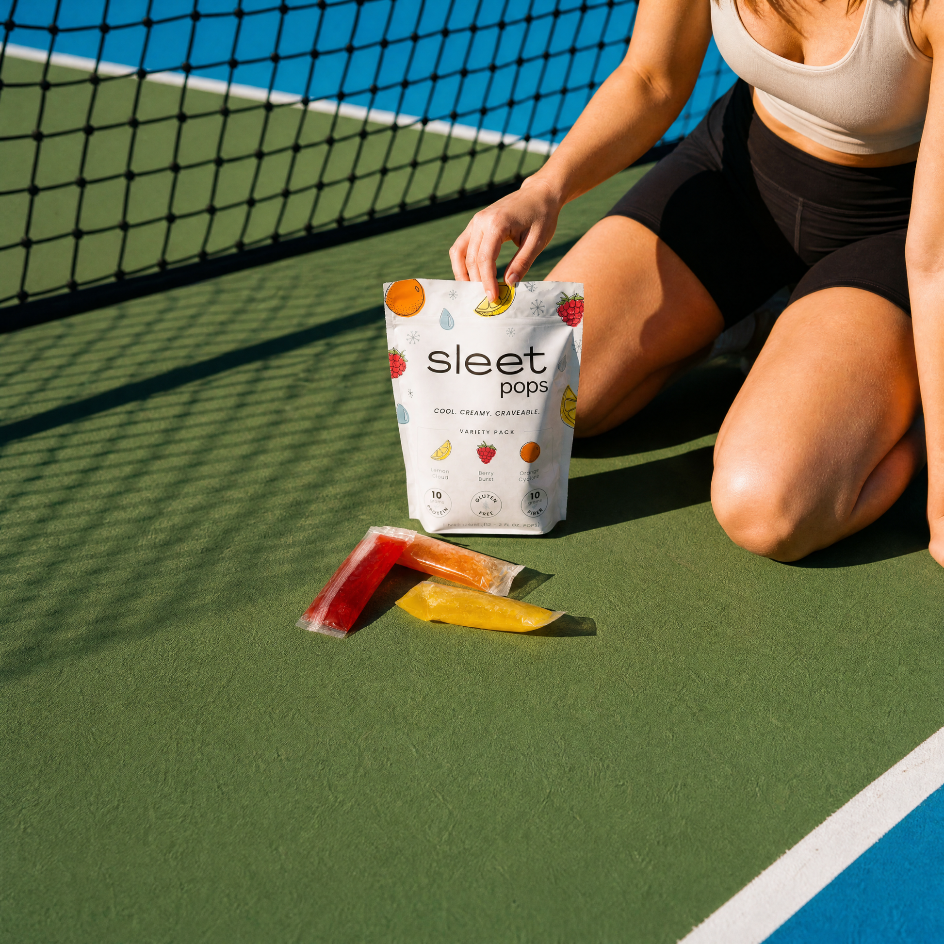 Person sitting on a tennis court with sleet pops packaging and popsicles.